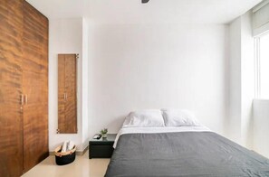 Een slaapkamer met een bed, een kledingkast, een nachtkastje en een kleine plant.