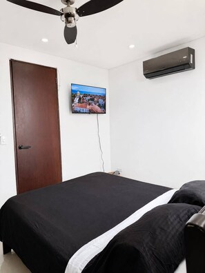 Ein Schlafzimmer mit einem Bett, einem Deckenventilator, einer Klimaanlage und einem an der Wand montierten Fernseher.