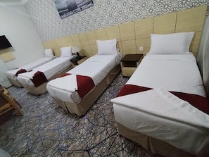 A hotel room with two single beds and a larger bed, all with white linens and red pillows. The room has a patterned wall and a tiled floor. - Safeer Almisk Hotel Mecca (Makkah)
