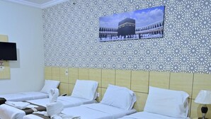 A hotel room with three beds, a television mounted on the wall, and a patterned wall. - Safeer Almisk Hotel Mecca (Makkah)