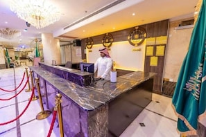 A hotel reception area with a marble counter, red stanchions, and a receptionist. - Safeer Almisk Hotel Mecca (Makkah)
