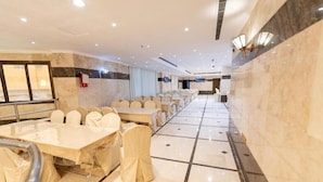 A hotel conference room with multiple tables and chairs, marble walls, and a tiled floor. - Safeer Almisk Hotel Mecca (Makkah)
