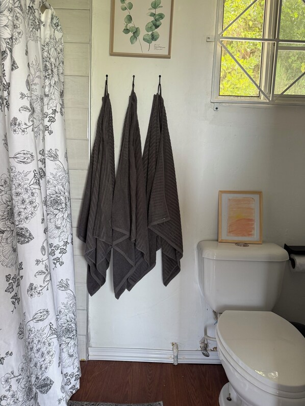 A bathroom with a shower curtain, three towels hanging, a framed botanical print, and a toilet.