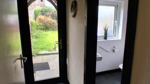 A hallway leading to a bathroom with a window, a door, and a small plant. - Cosy 3-bedroom Townhouse With Garden (Wexford)