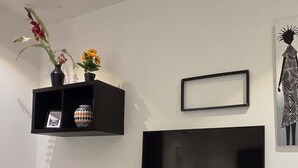 A modern living room with a flat-screen TV mounted on a black entertainment unit, a small wooden stool, and a brown and white rug. - EBS PROPERTIES (Accra)