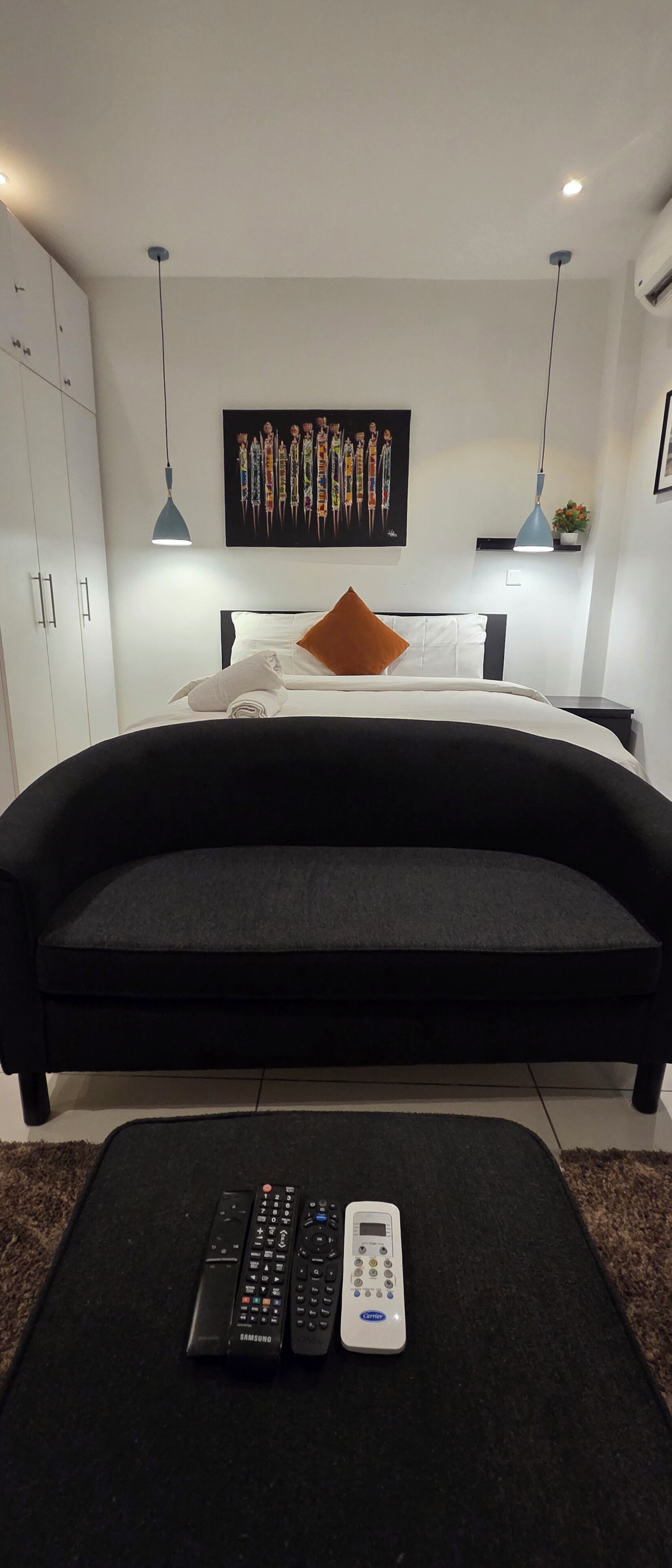 Une chambre moderne avec un grand lit, un canapé noir et une œuvre d’art accrochée au mur.