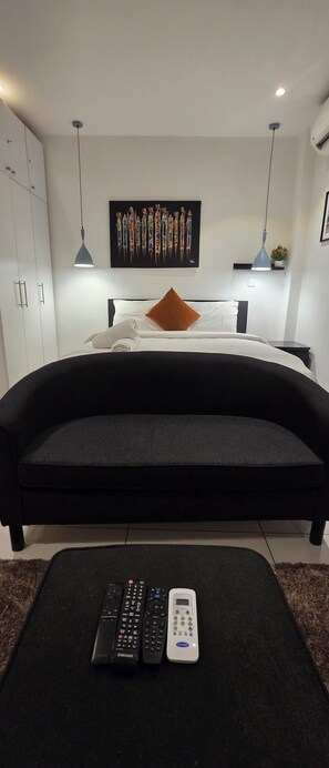 Un dormitorio moderno con una cama grande, un sofá negro y una obra de arte colgada en la pared.