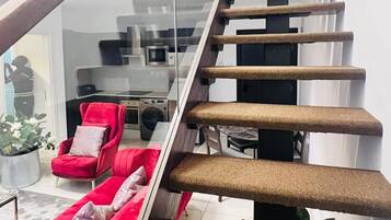 Una escalera moderna con barandilla de vidrio que conduce a una sala de estar con un sofá rojo y una mesa de comedor.