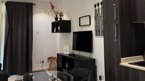 A modern living room with a glass coffee table, black chairs, a wooden dining table, a TV on the wall, and a dark wooden cabinet. - EBS PROPERTIES (Accra)