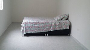 Una cama individual con una colcha estampada en una habitación con paredes lisas y suelo de baldosas.