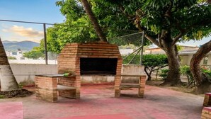 Un horno de ladrillo al aire libre con una mesa y sillas, rodeado de árboles y una valla.