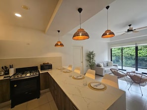 A modern kitchen with a central island, dining area with chairs, and a view of greenery outside. - Beachfront Apartment, Family-Friendly Atmosphere, Just a Few Steps from the Ocean. (San Carlos)