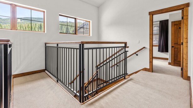 Ein geräumiges Zimmer mit hoher Decke, einer Holztreppe mit schwarzer Geländer und großen Fenstern mit Blick auf ein bewaldetes Gebiet.
