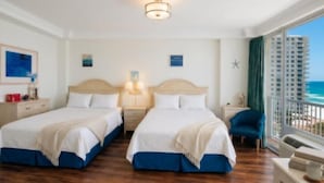 A hotel room with two beds, a view of the ocean, and a balcony with a railing.
