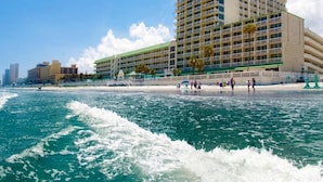 A beachfront hotel with multiple balconies, a pool area, and a view of the ocean.