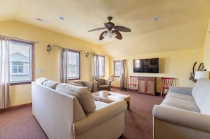 A living room with beige sofas, a coffee table, a TV, and a ceiling fan. - The Sea Spirit-KDH MP 7, Oceanside, Elevator, Pool, Hot Tub, Pets OK, YR Flex Stays (Kill Devil Hills)