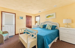 A bedroom with a bed, a nightstand, a dresser, a chair, and a door. - The Sea Spirit-KDH MP 7, Oceanside, Elevator, Pool, Hot Tub, Pets OK, YR Flex Stays (Kill Devil Hills)