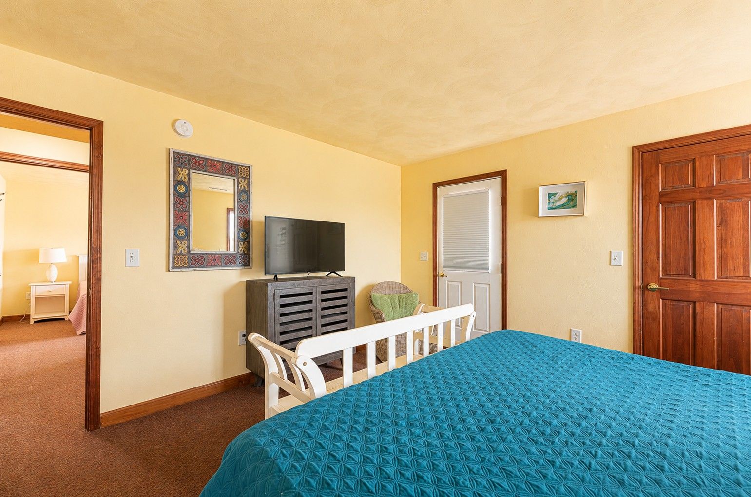 Une chambre à coucher avec un lit, un téléviseur posé sur un meuble, une porte et un miroir fixé au mur.