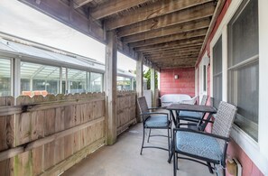 Ein überdachter Patio-Bereich mit Holzzaun, einem Tisch mit Stühlen und einem Gewächshaus im Hintergrund.