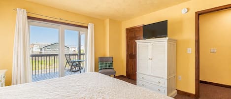 Ein Schlafzimmer mit einem großen Bett, einem Sessel, einem Kleiderschrank und einem Balkon mit Tisch und Stühlen.