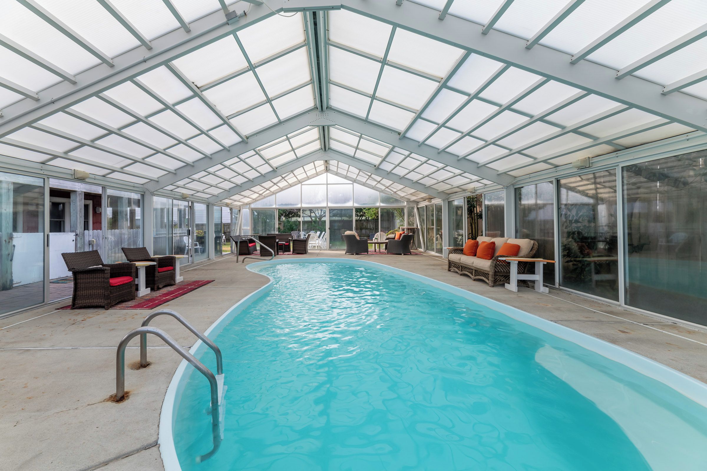 A covered swimming pool with lounge chairs and a glass enclosure.