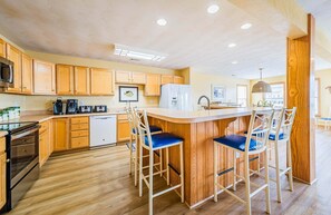 A kitchen with wooden cabinets, a built-in microwave, a refrigerator, and a bar area with stools. - Captains Choice-KDH MP 7, Oceanside, Pool, Hot Tub, Pets OK, YR Flex Stays (Kill Devil Hills)