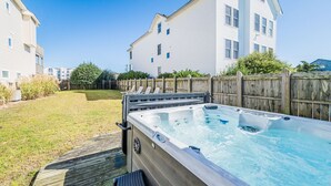 Ein Whirlpool in einem Hinterhof mit einer Holzterrasse, einem Holzzaun und einem weißen Gebäude im Hintergrund.
