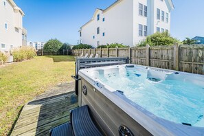 A hot tub in a backyard with a wooden deck, a wooden fence, and a white building in the background. - Captains Choice-KDH MP 7, Oceanside, Pool, Hot Tub, Pets OK, YR Flex Stays (Kill Devil Hills)