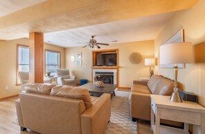 A spacious living room with a fireplace, leather sofas, a television, and a ceiling fan. - Captains Choice-KDH MP 7, Oceanside, Pool, Hot Tub, Pets OK, YR Flex Stays (Kill Devil Hills)