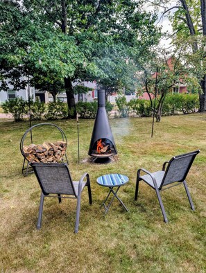 An outdoor seating area with a black fire pit, two chairs, and a small table.