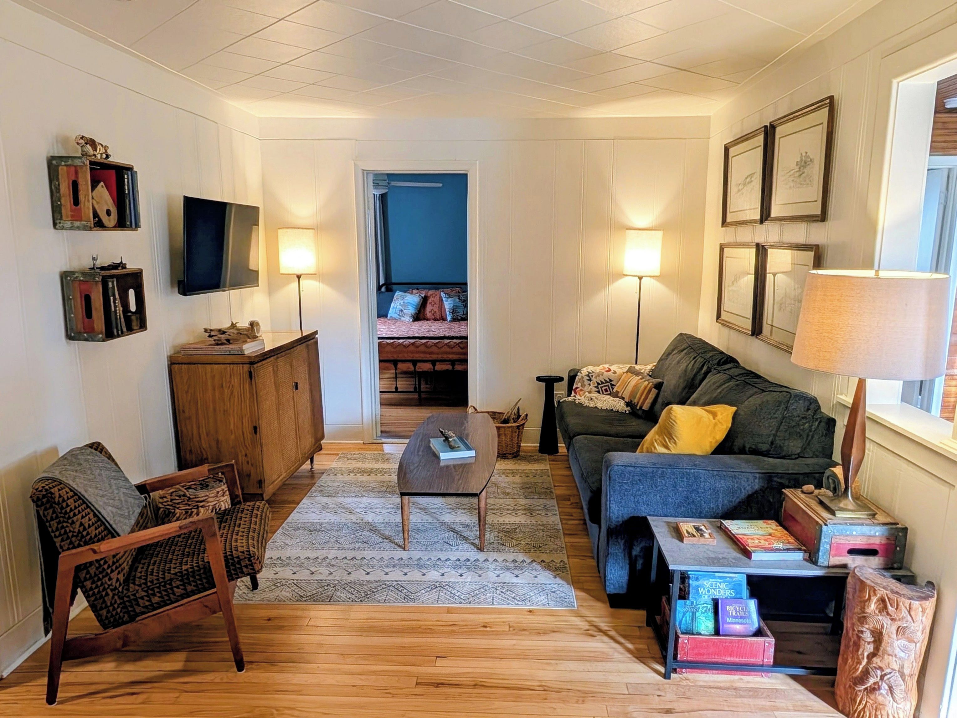 A cozy living room with a sofa, armchairs, a coffee table, and a television. There is a bookshelf with books and decorative items.