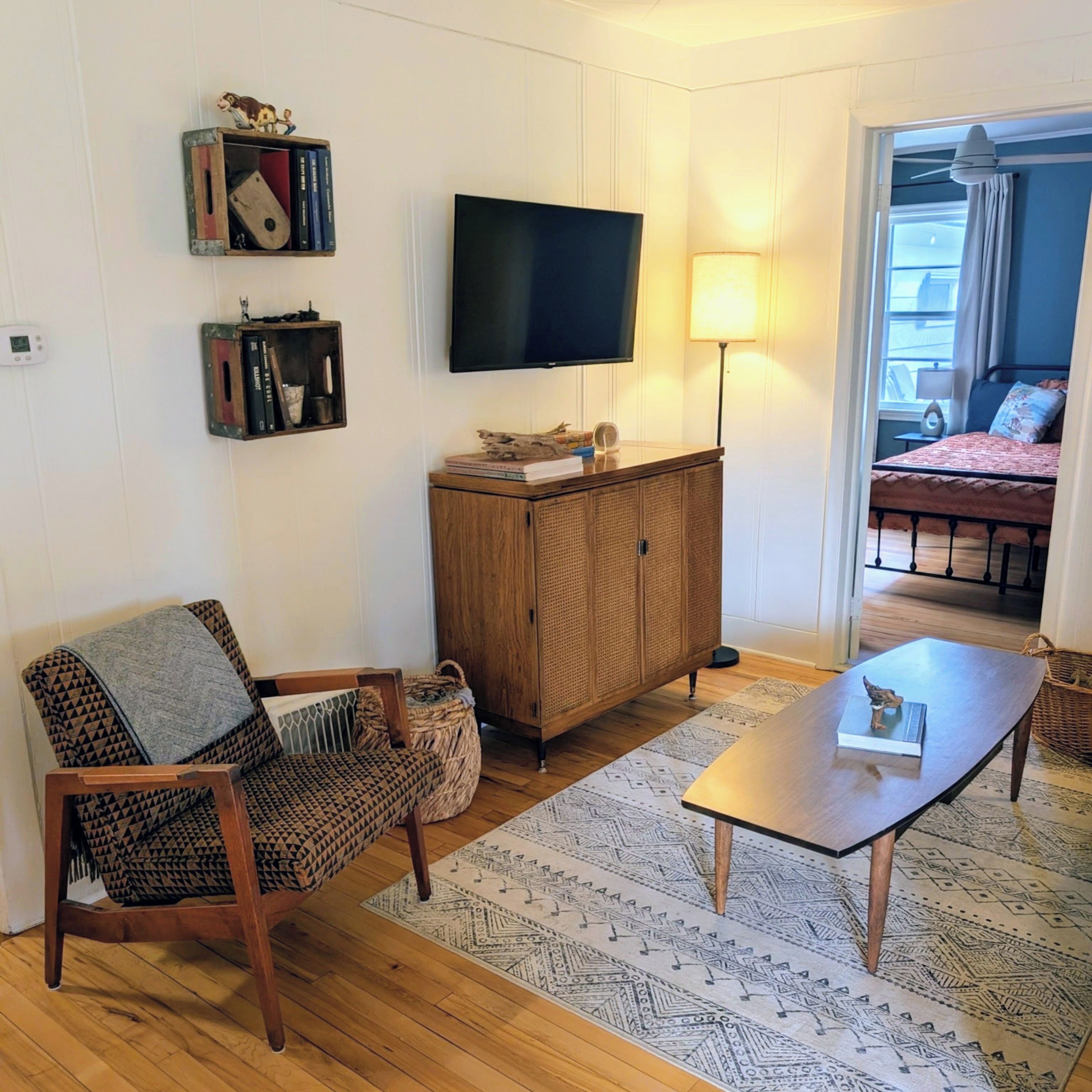 Ein Wohnzimmer mit Fernseher, einem Holzkabinett, einem gemusterten Teppich und einer Couch.