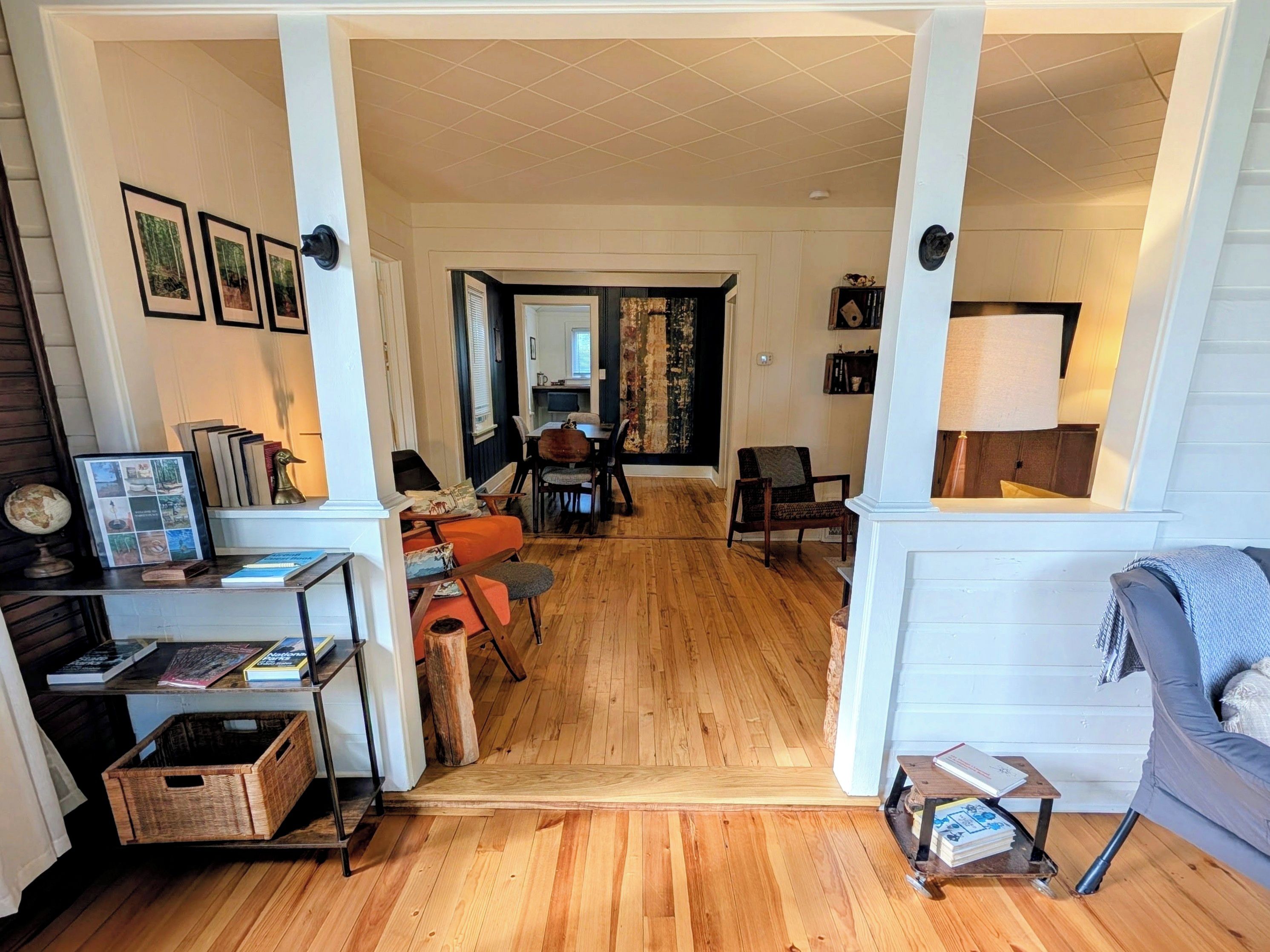 A spacious living area with a wooden floor, a sofa, a coffee table, and a dining table with chairs. There is a bookshelf with books and a globe.