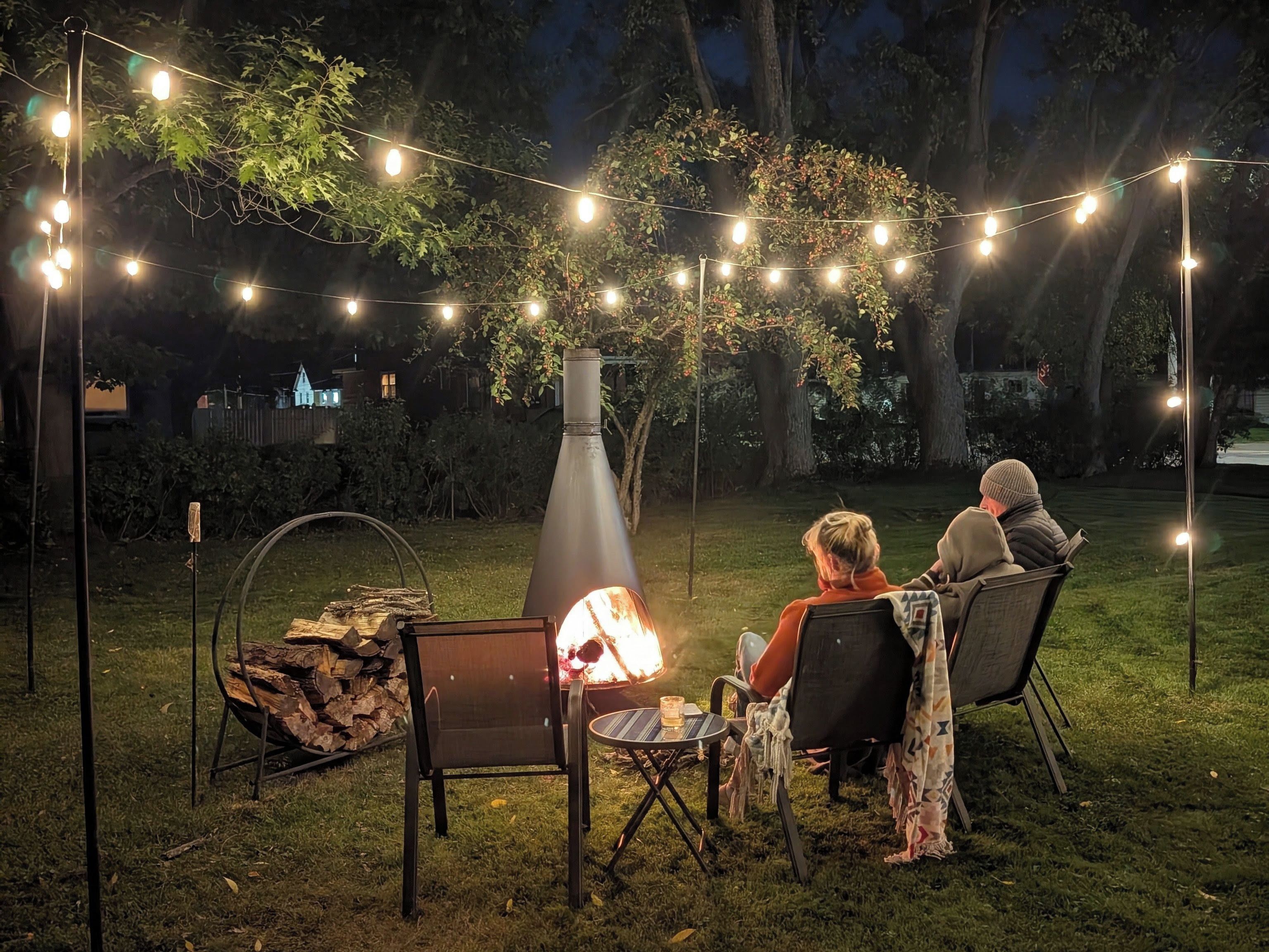 An outdoor seating area with a fire pit, string lights, and a metal chimney structure.