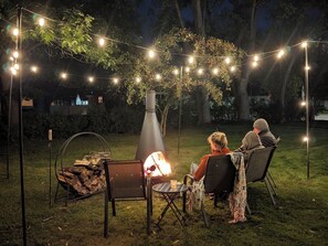 An outdoor seating area with a fire pit, string lights, and a metal chimney structure.