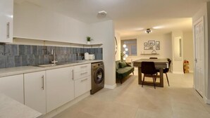 A modern kitchen with a built-in washing machine, a dining area with a table and chairs, and a living space with a sofa. - Southsea Luxury Apartment with Hot tub   (Portsmouth)