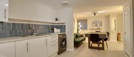 Una cocina moderna con lavadora integrada, un comedor con mesa y sillas, y una sala de estar con sofá.