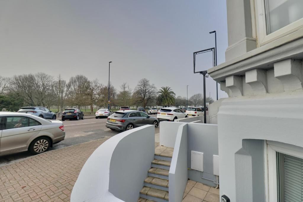 A parking area with cars, a building with a white facade, and a clear sky.