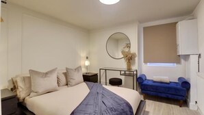 A bedroom with a bed, bedside table, lamp, mirror, and a blue sofa. - Southsea Luxury Apartment with Hot tub   (Portsmouth)