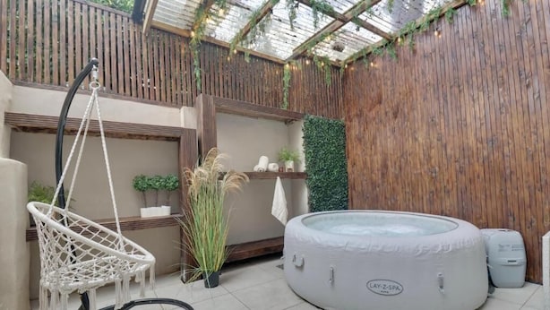 A spa area with a hot tub, a hanging chair, and a wooden wall with greenery. - Southsea Luxury Apartment with Hot tub   (Portsmouth)