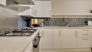 A modern kitchen with white cabinetry, a gas stove, and a stainless steel range hood. - Southsea Luxury Apartment with Hot tub   (Portsmouth)