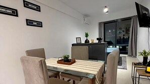 Et moderne spiseområde med et glasbord, fire stole og et mørkt konsolbord med en plante og billedramme.