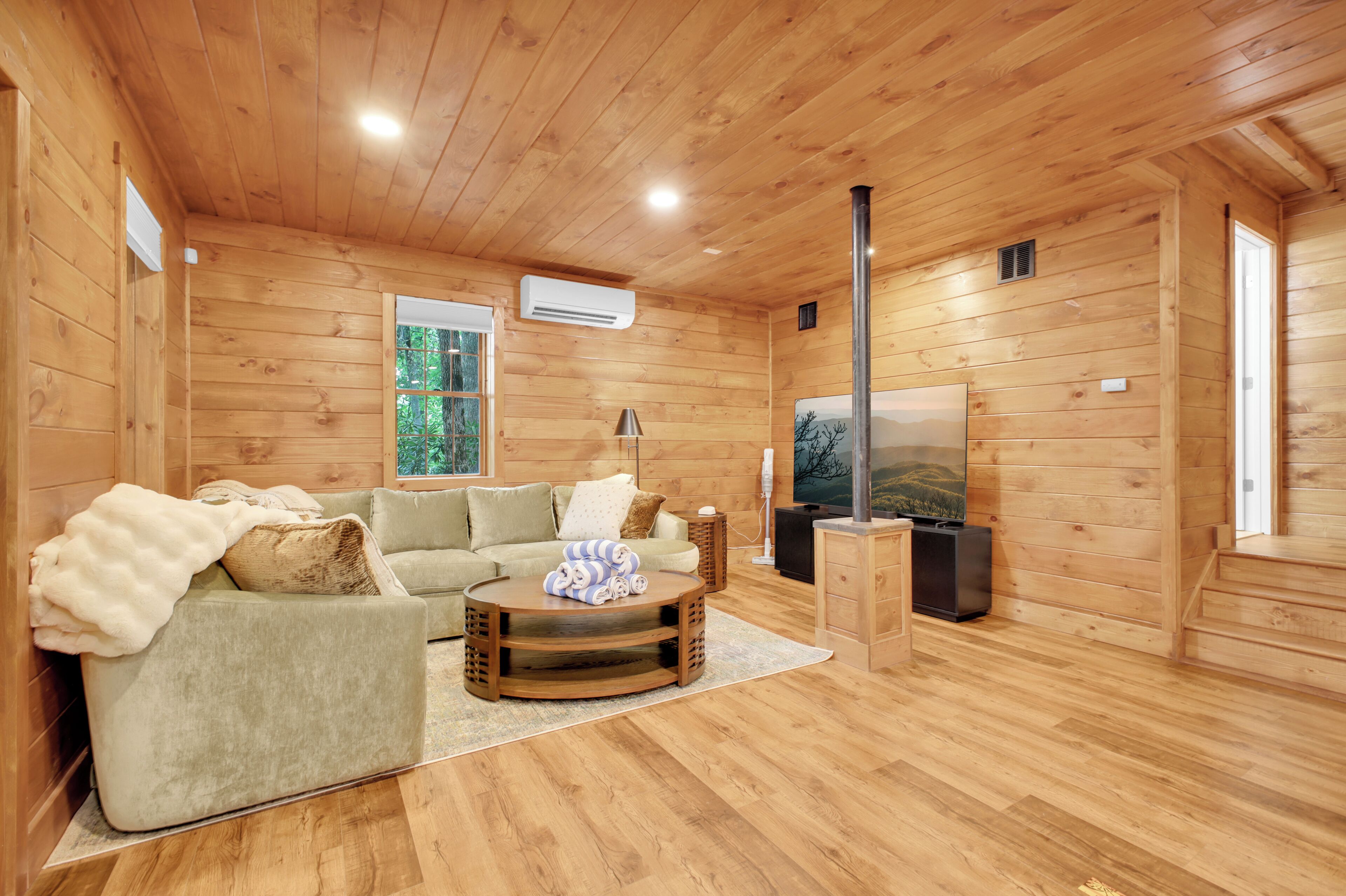 A wooden-paneled room with a sofa, a coffee table, a TV, and a window with a view of trees.