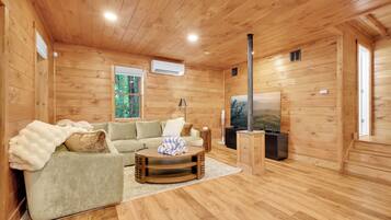 A wooden-paneled room with a sofa, a coffee table, a TV, and a window with a view of trees.
