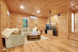 A wooden-paneled room with a sofa, a coffee table, a TV, and a window with a view of trees.