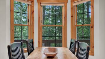 Ein Essbereich mit Holztisch und -stühlen, großen Fenstern mit Blick auf Bäume und einer Holzausstattung an der Decke.
