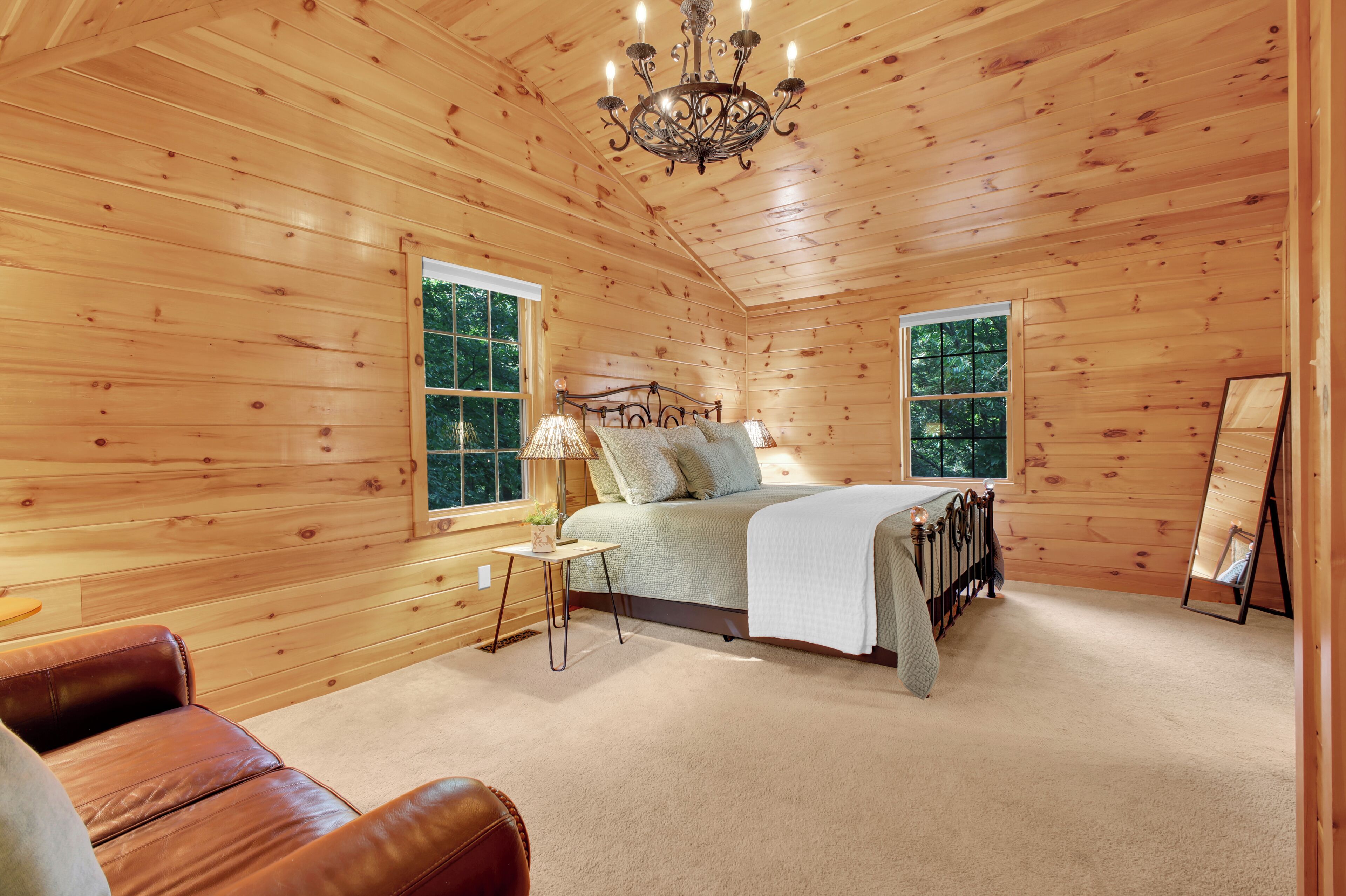 A wooden cabin bedroom with a bed, a nightstand, a lamp, and a large window.