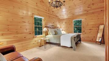 A wooden cabin bedroom with a bed, a nightstand, a lamp, and a large window.