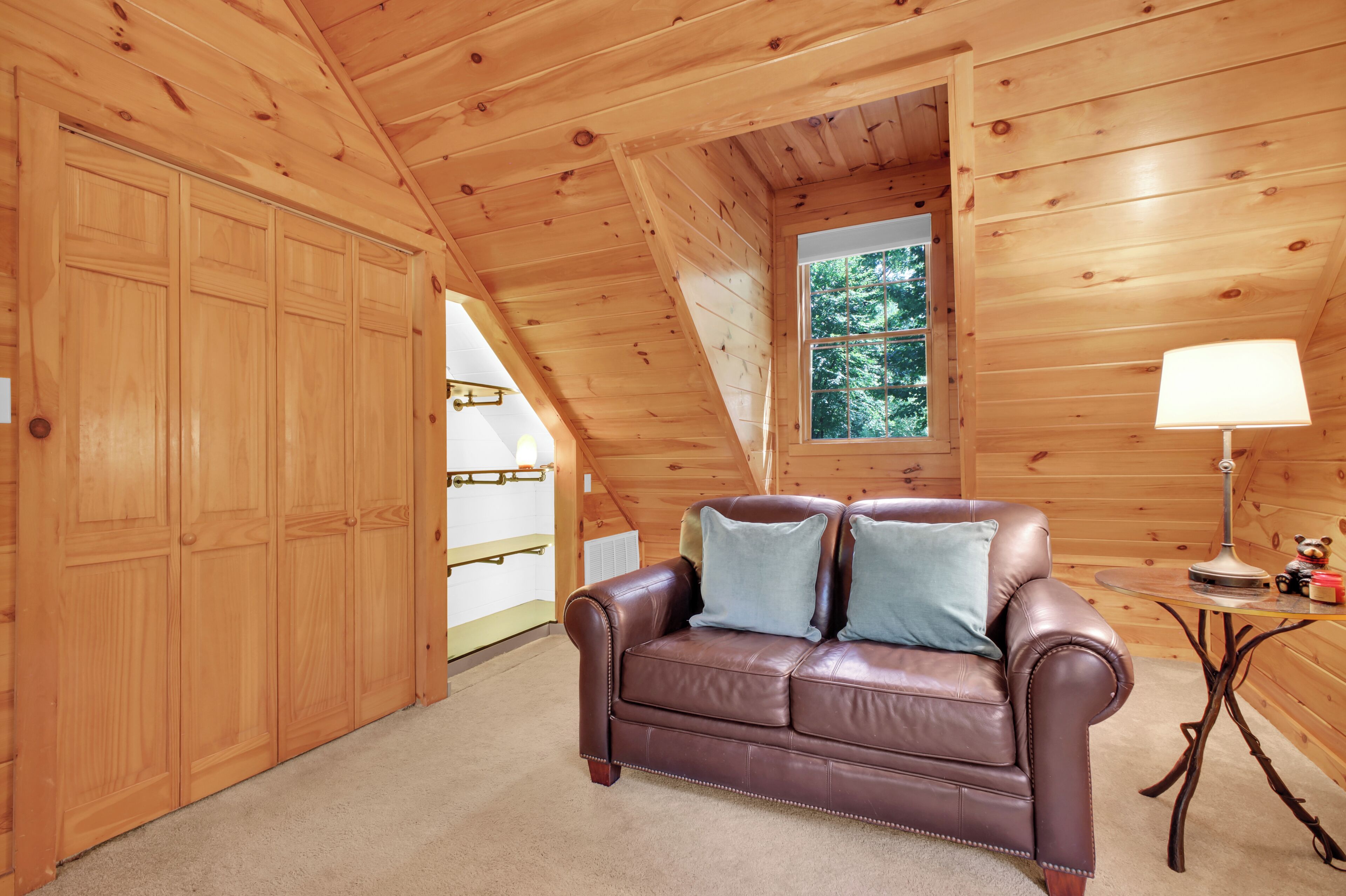 Una habitación acogedora con un sofá de cuero marrón, techo de madera y ventana con vistas a árboles.