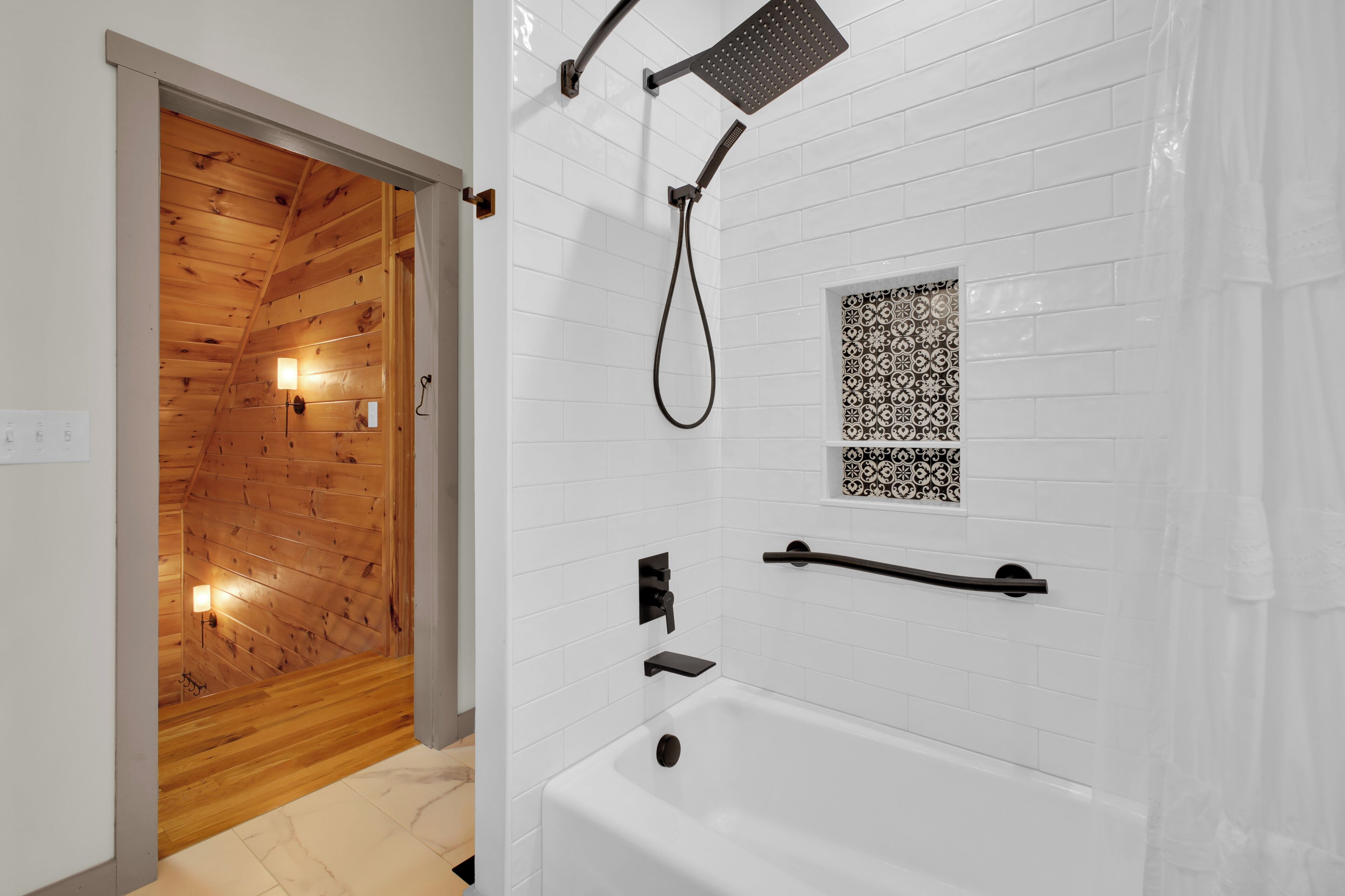 Un bagno moderno con soffitto in legno, pareti rivestite di piastrelle bianche, una vasca, una doccia con soffione manuale e un piccolo pannello decorativo in piastrelle.